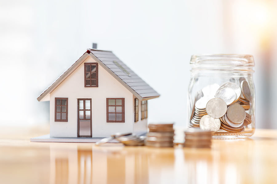 An HOA house with money in a jar next to it on a table to represent an HOA lockbox for sending money from banks to HOA homes